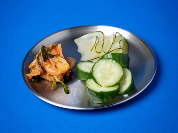 Tsukemono num prato de inox: kimchi, pepino e nabo